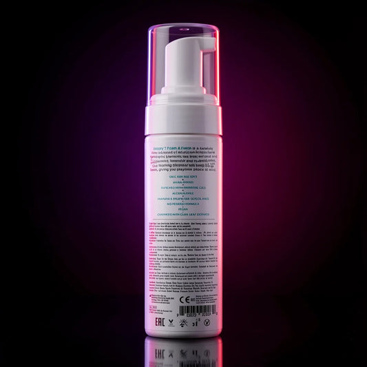 The back of a white pump bottle with a clear cap, illuminated by pink and purple lighting against a dark background with a reflection below.