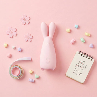 Pink rabbit vibrator flatlay with cherry blossoms, pastel star confetti, rainbow washi tape, and kawaii bunny notebook