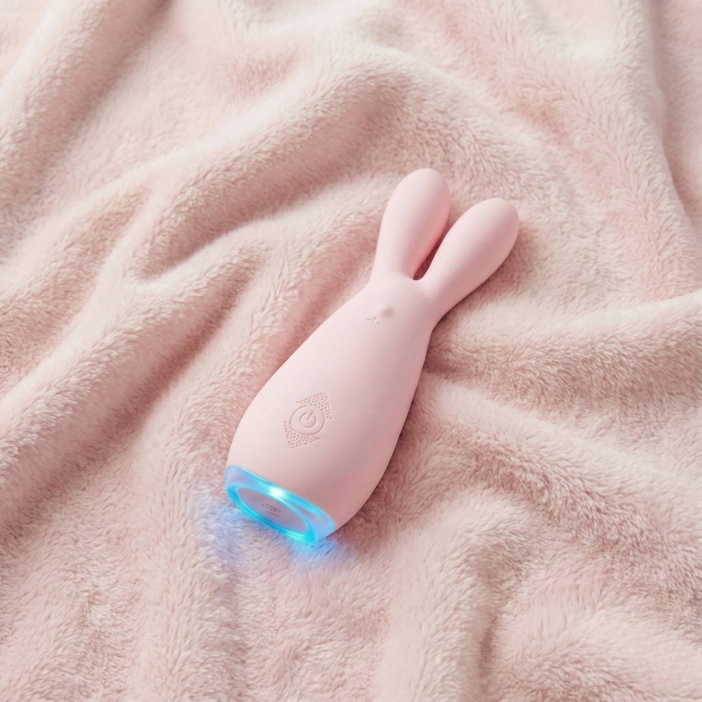 Pink dual motor bunny vibrator with glowing blue LED light displayed on soft pink fleece blanket