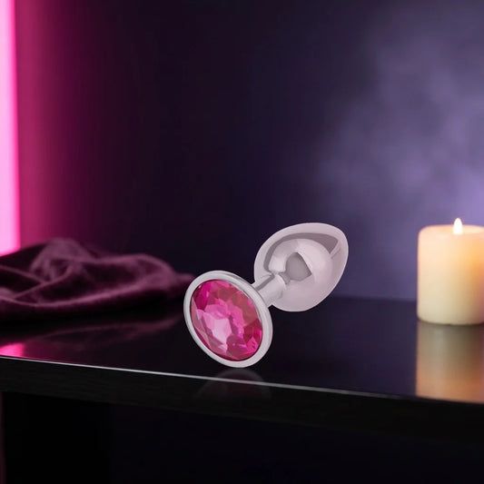 Silver plug with a pink jewel base on a dark shelf