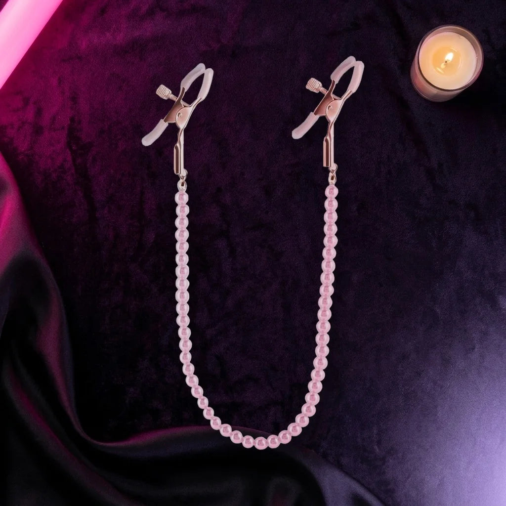 Rose gold nipple clamps with a pink pearl chain on dark velvet