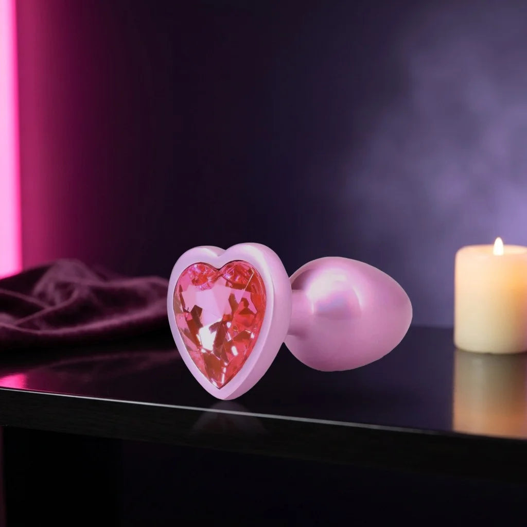 Pink metal plug with a heart-shaped pink jewel on a dark shelf