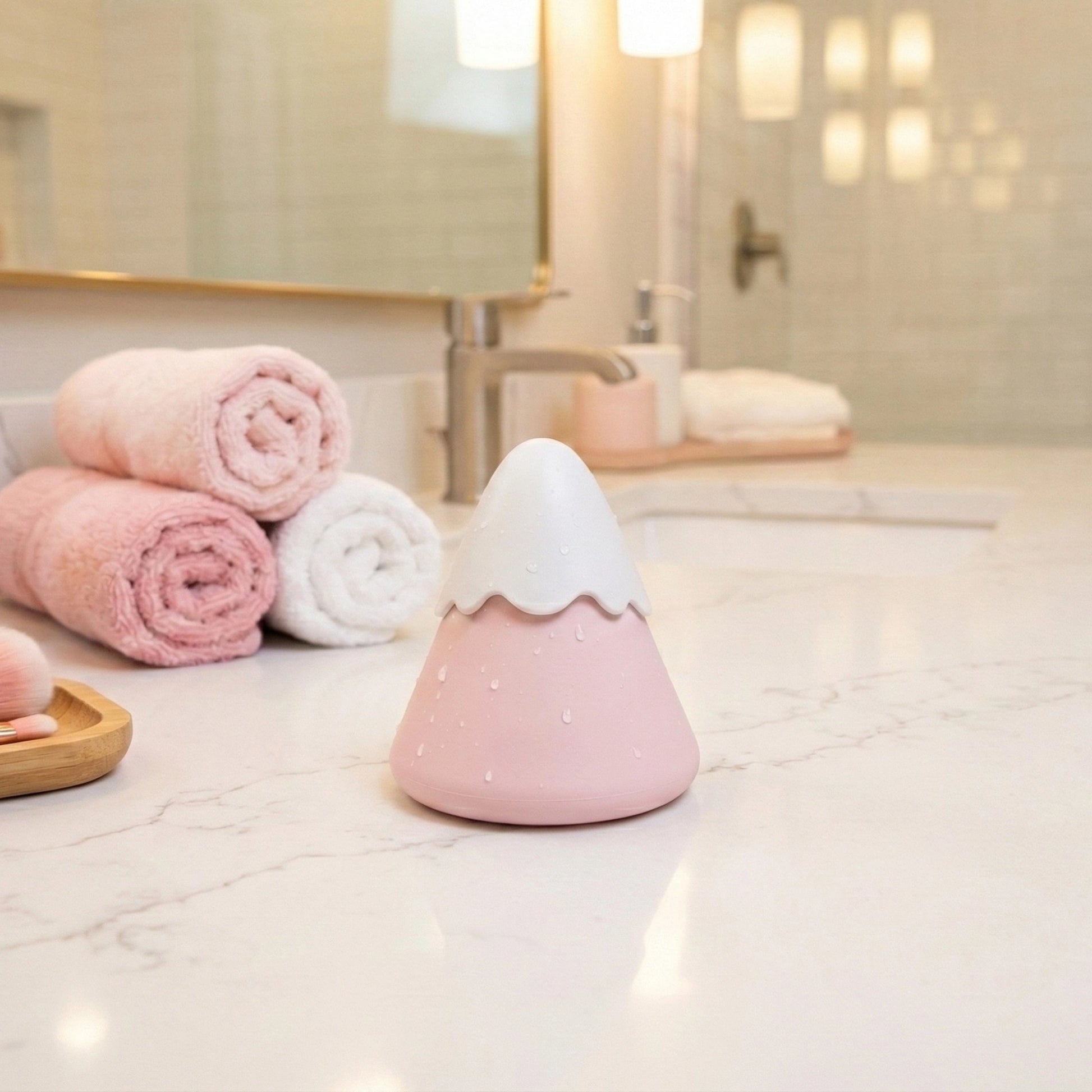 Pink waterproof Fuji volcano air pulse suction toy on white marble bathroom counter with rolled towels, mirror background