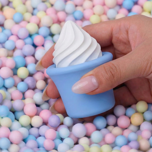 Hands holding blue Sprinkles soft serve cone clitoral vibrator sex toy against pastel candy ball pit background